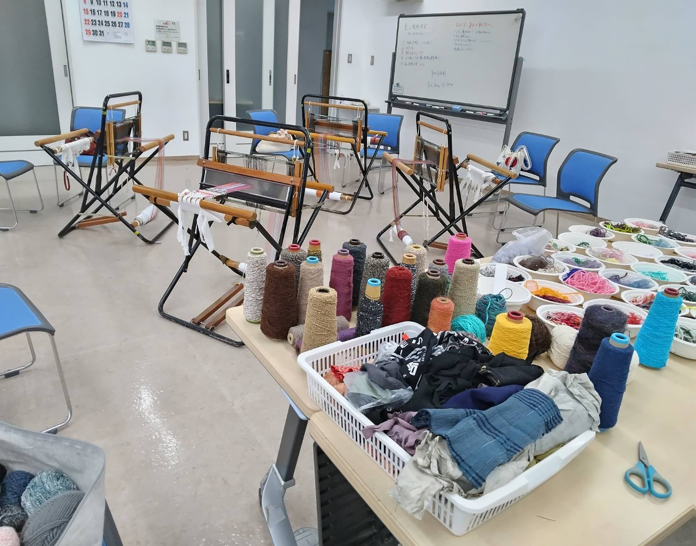 機織り機4台とテーブルの上に並べられた沢山の糸